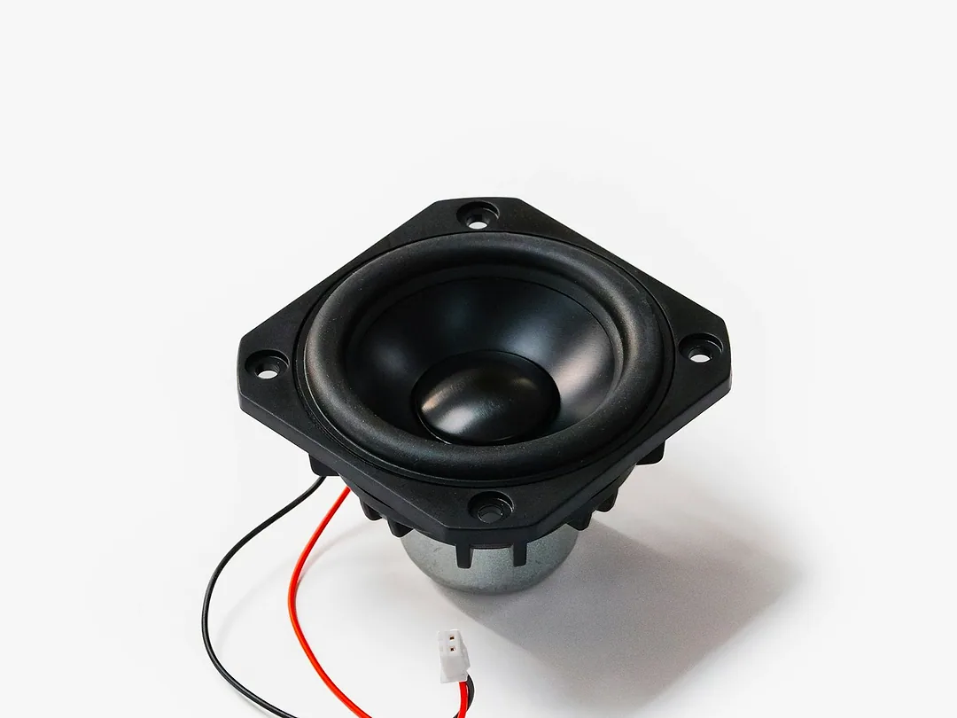A car door speaker with its red and black lead, on white