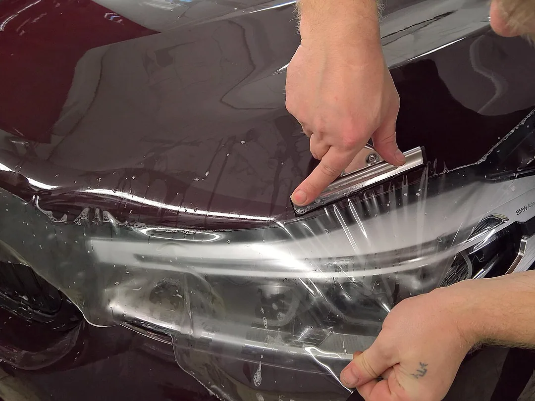 Hands smoothing clear protection film onto a car's bonnet